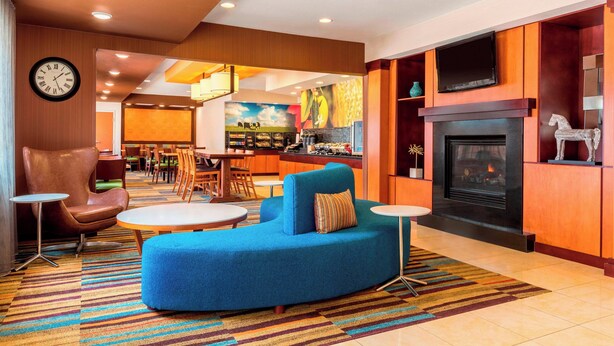 A modern hotel lobby with a blue sofa, a fireplace, a dining area, and a kitchen in the background. - Fairfield Inn & Suites Abilene (Abilene)