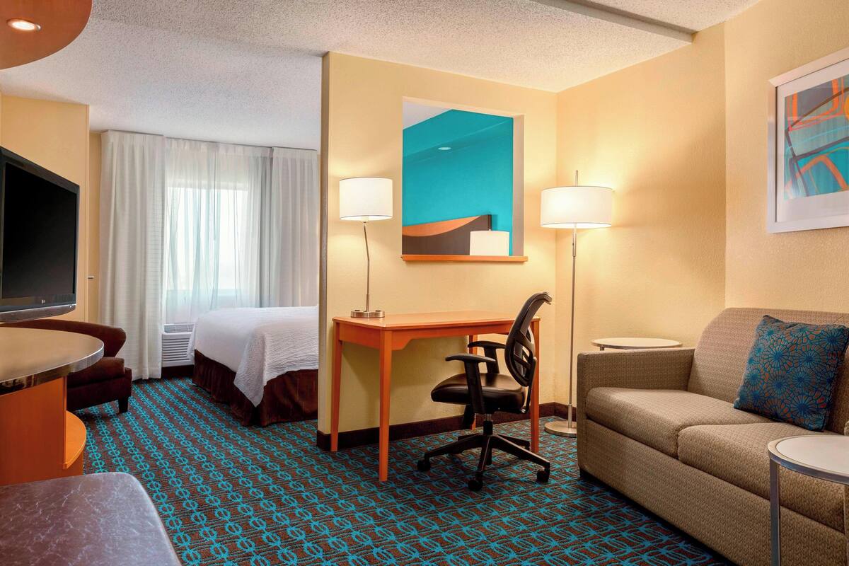 A hotel room with a bed, desk, chair, sofa, and a TV.
