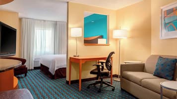 A hotel room with a bed, desk, chair, sofa, and a TV.