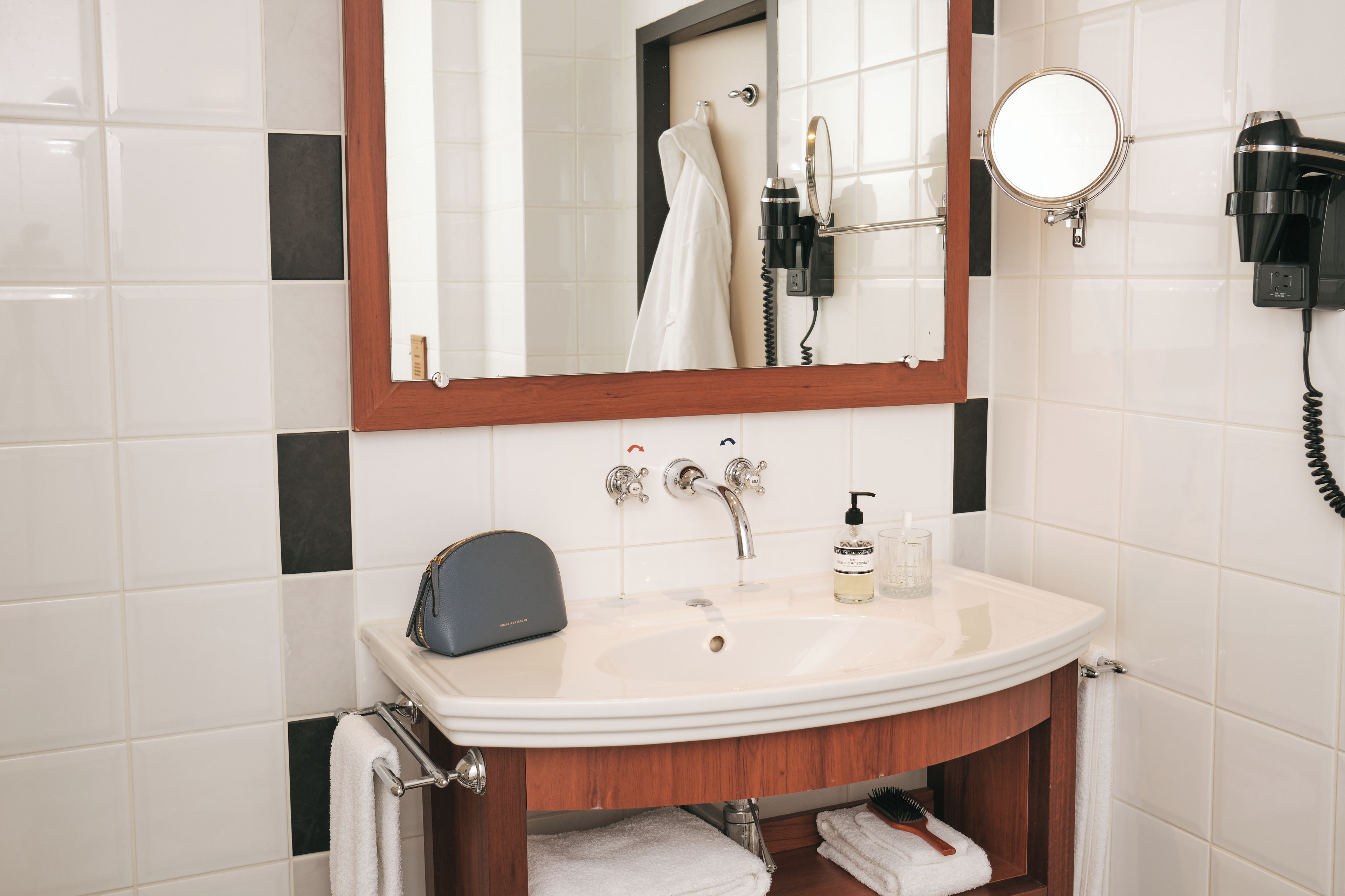 Un baño con lavamanos blanco, espejo, toallero, secador de pelo y teléfono.