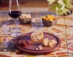 Una tabla de madera con queso, uvas y galletas sobre una mesa con mantel estampado.