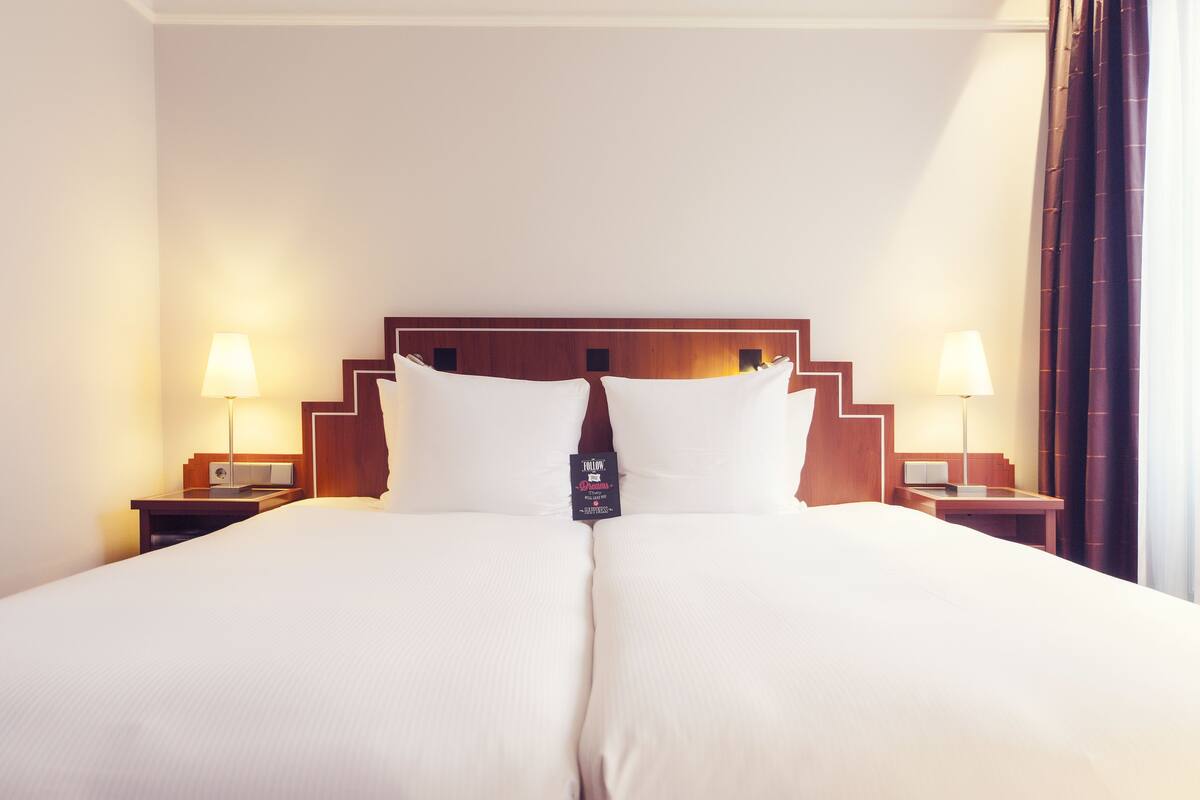 A hotel room with a large bed, two bedside tables, lamps, and a headboard with a logo.