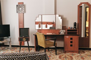 A hotel room with a bed, a desk, a chair, a television, a clock, and a mirror.