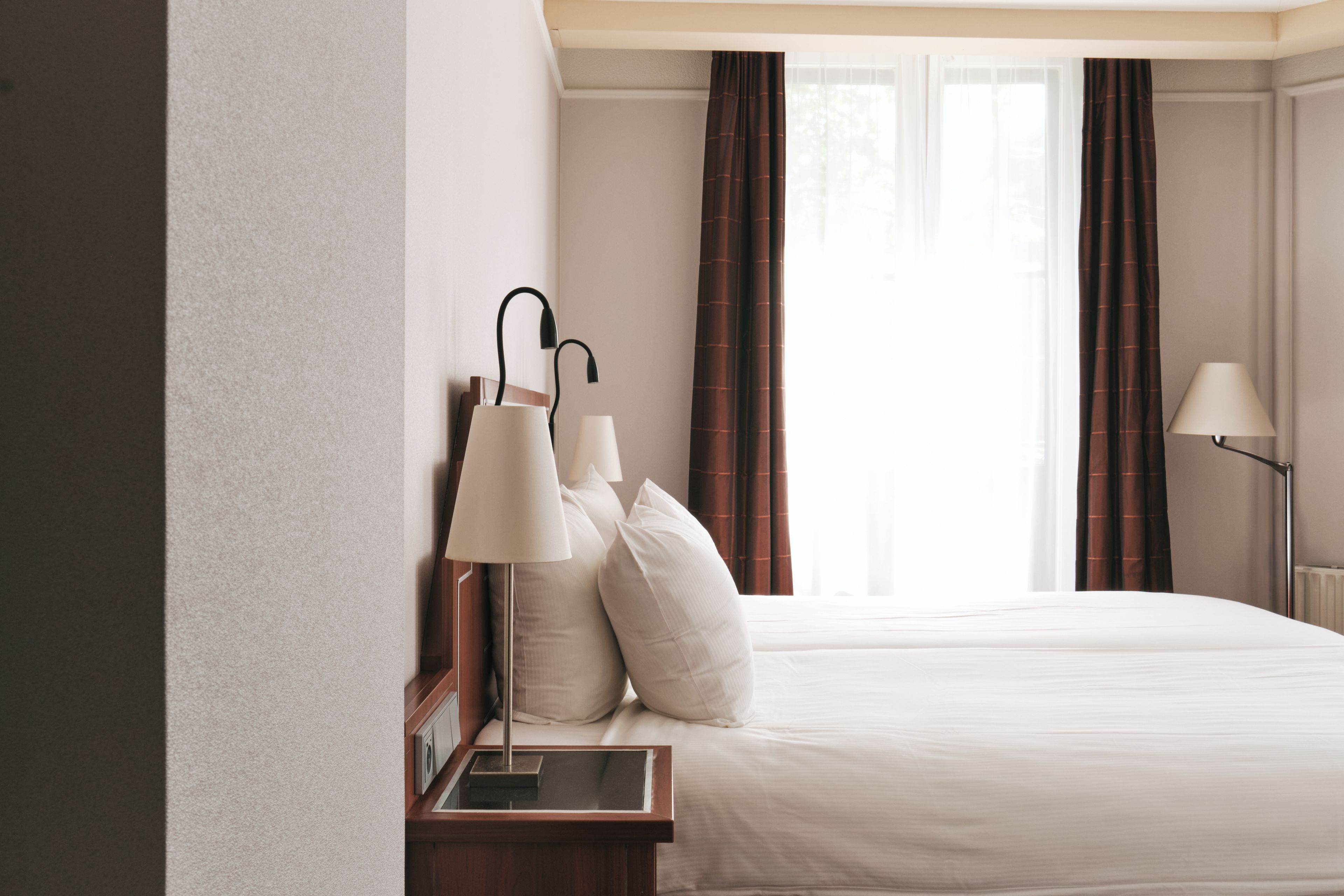 Une chambre d’hôtel avec un lit, deux lampes de chevet, une table de nuit et une fenêtre avec des rideaux.