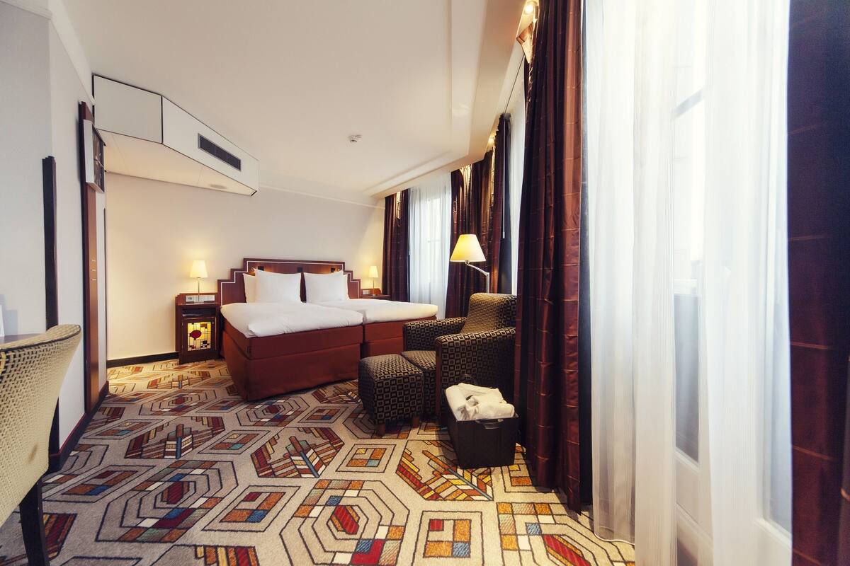 A hotel room with a bed, a chair, a small table, and a lamp.