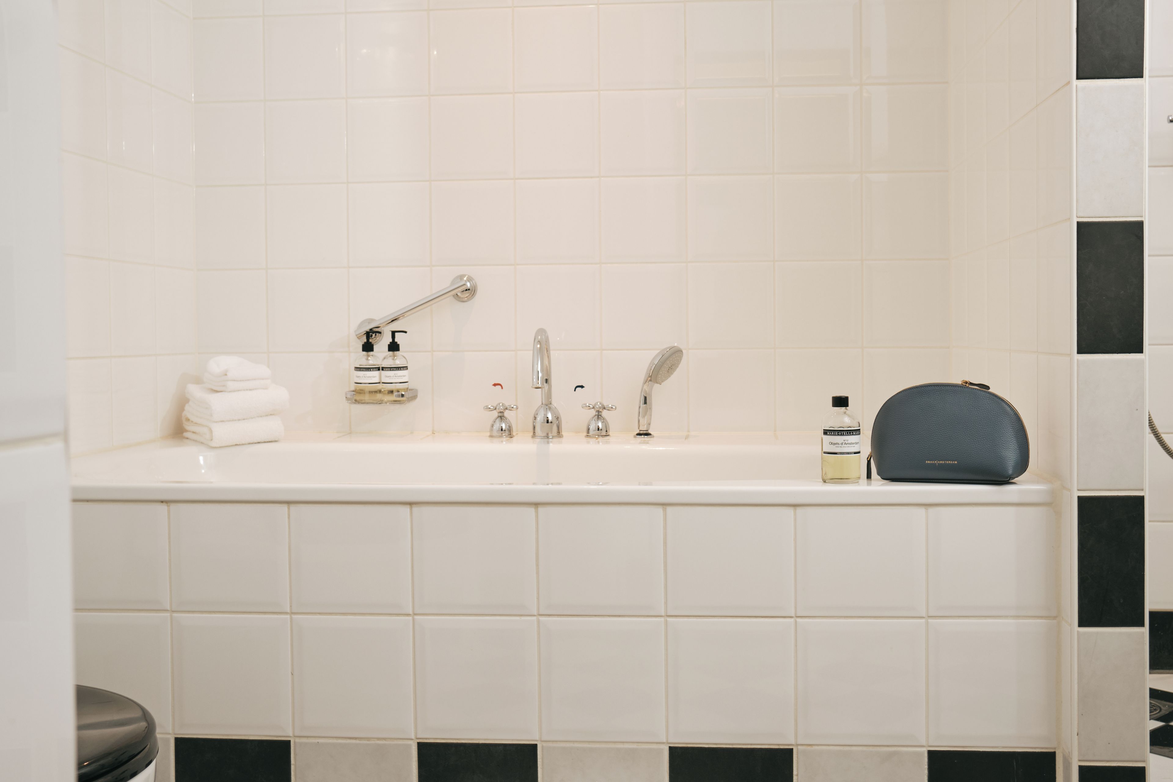 Een badkamer met een witte badkuip, een stapel handdoeken, een fles handzeep, een fles shampoo en een toilettas.