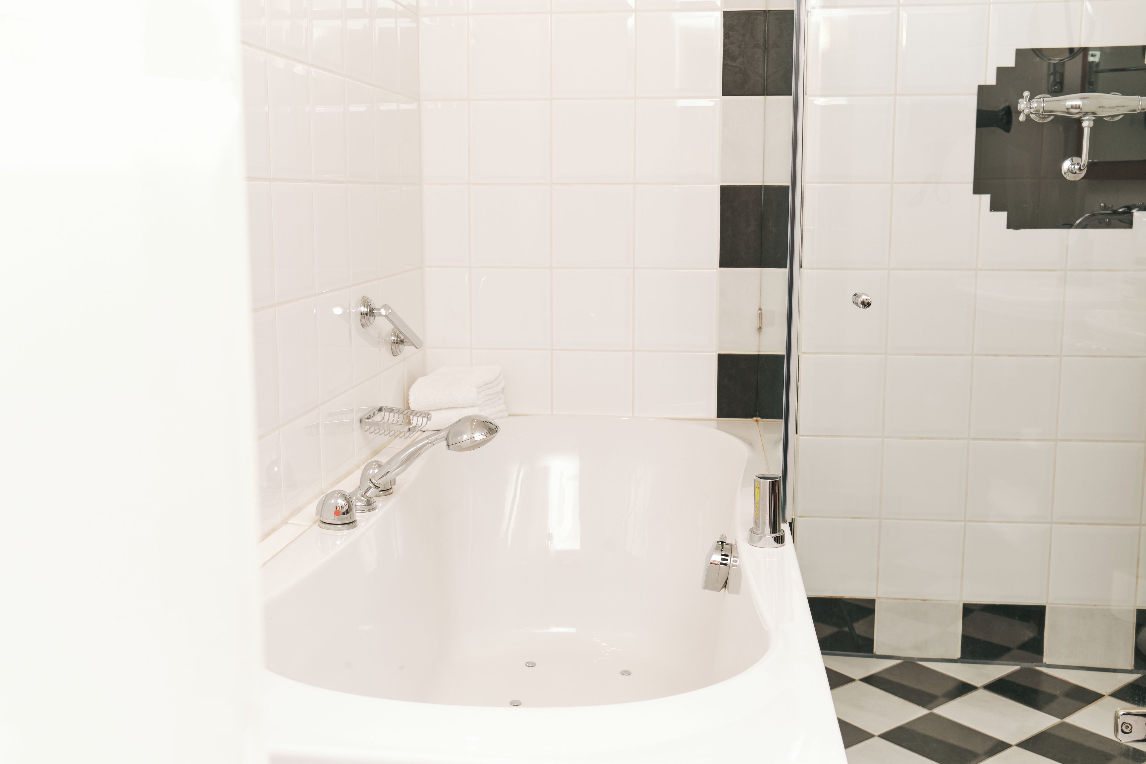 A bathroom with a white bathtub, a glass shower enclosure, and a checkered floor.