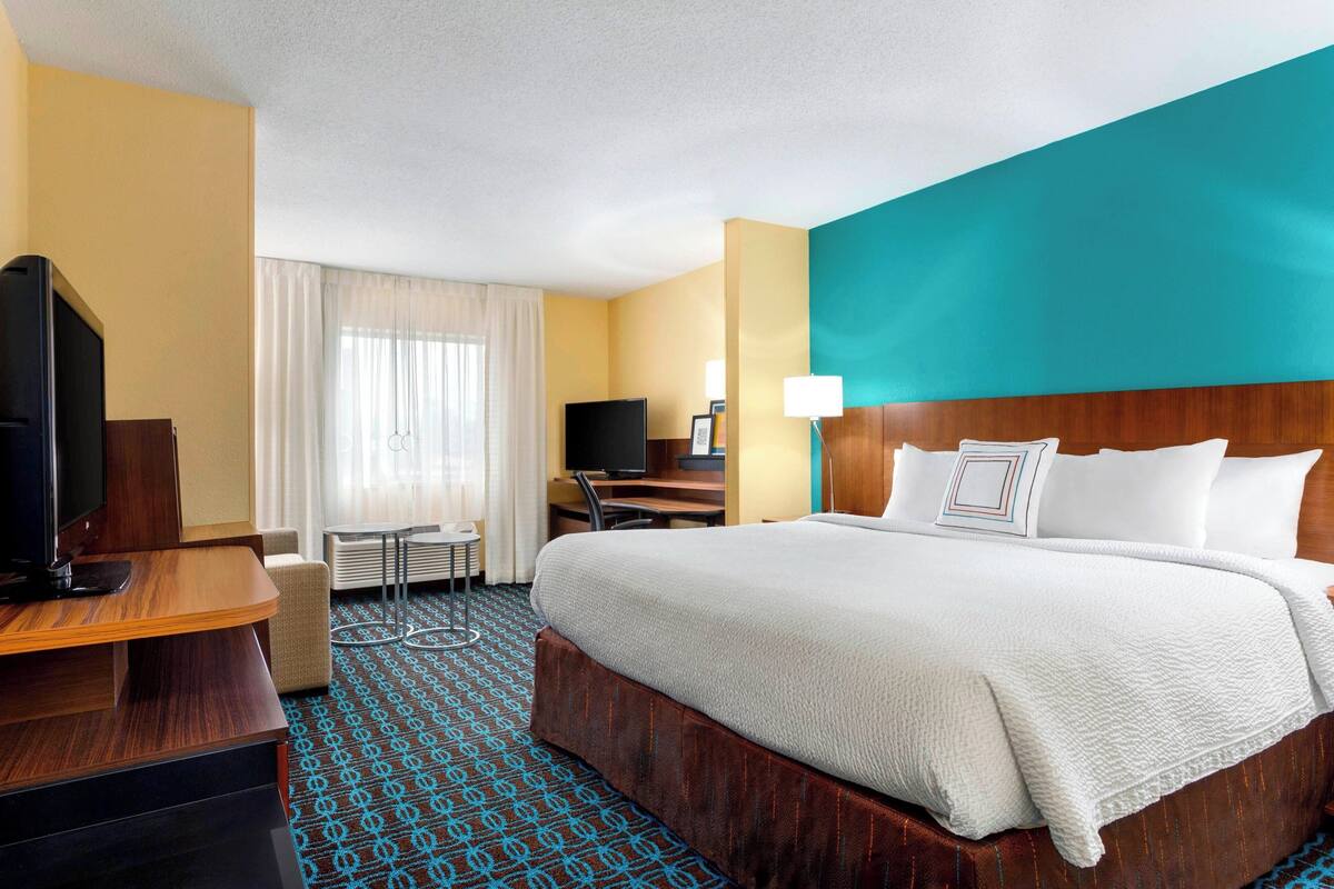 Hotelkamer met een groot bed, een bureau met een computer, een televisie en een raam met gordijnen.