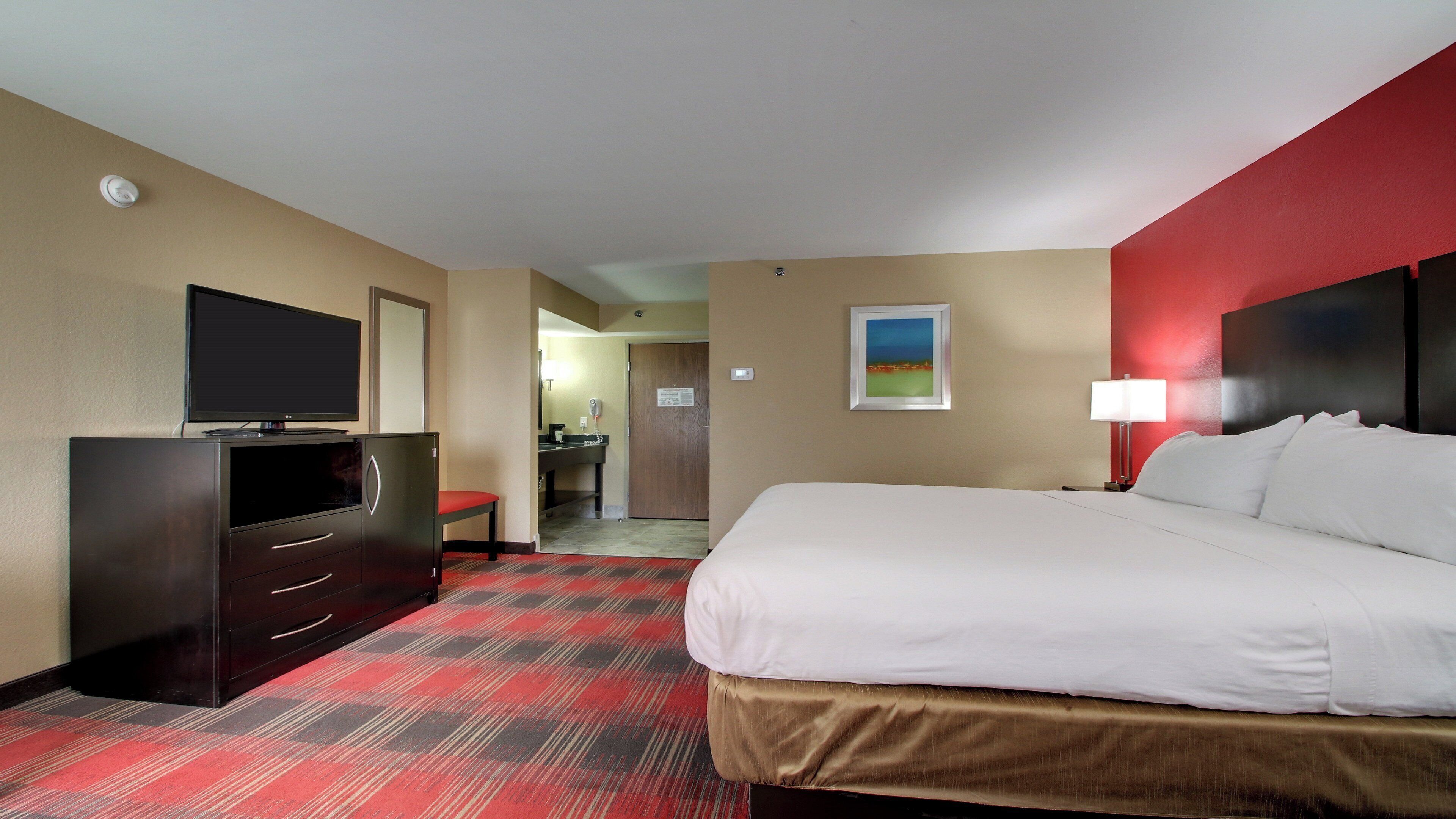 Habitación de hotel con cama, televisión, escritorio y baño visible a través de una puerta abierta.