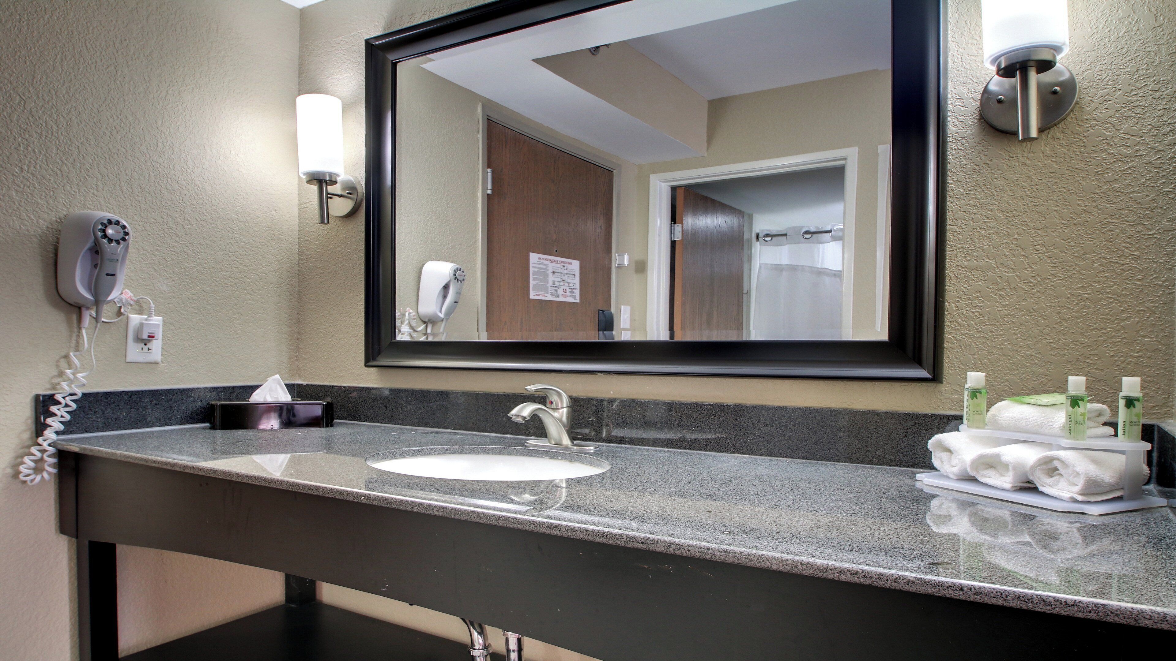Un baño de hotel con lavamanos, espejo, toallero y secador de pelo.