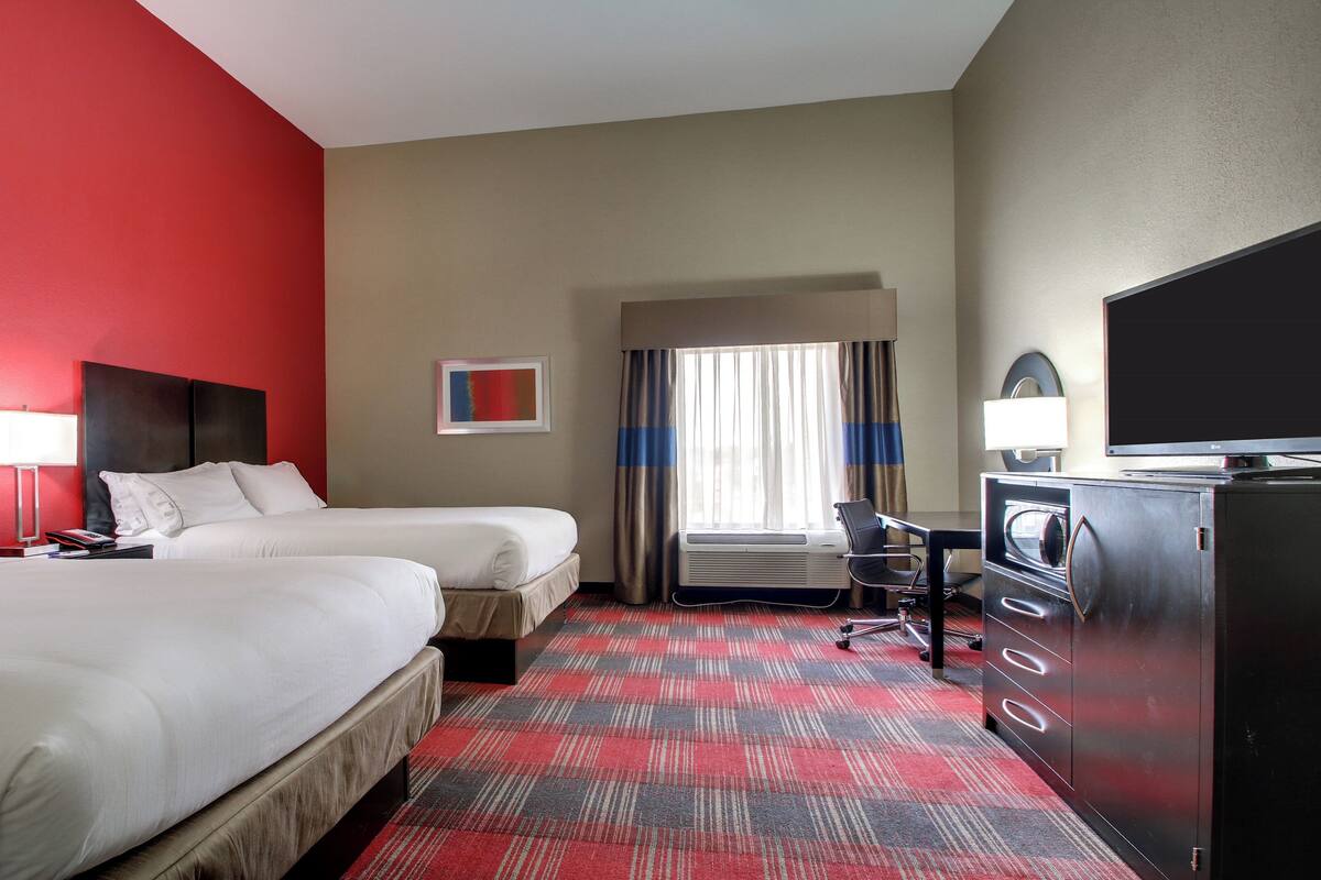 A hotel room with two beds, a desk, a television, and a window with curtains.