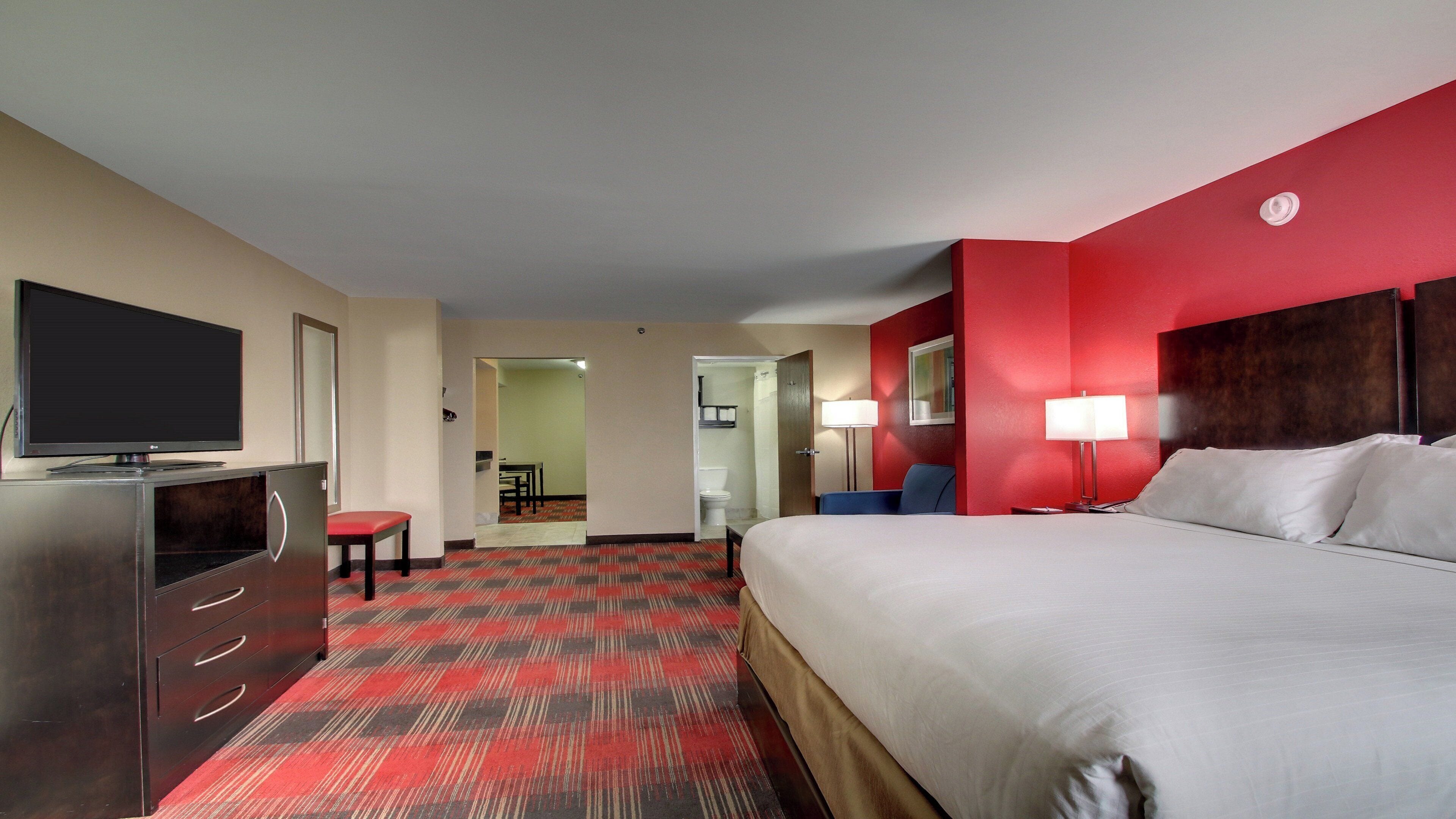 Habitación de hotel con cama, escritorio con televisor, una silla y baño visible a través de una puerta abierta.