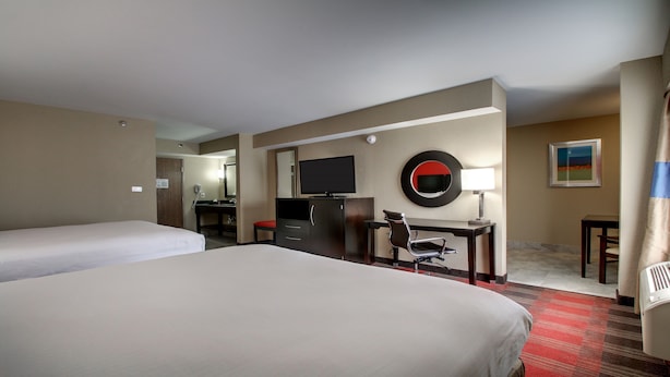 A hotel room with two beds, a desk with a chair, a television, a mirror, a lamp, and a painting on the wall. - Holiday Inn Express & Suites Jackson Downtown - Coliseum by IHG (Jackson)