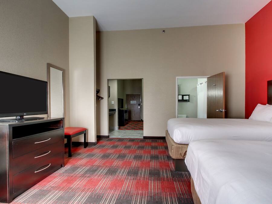 A hotel room with a bed, a TV, a desk, and a red carpet.