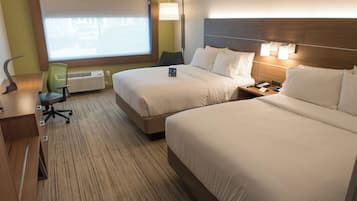 A hotel room with two beds, a desk, a chair, a lamp, and a window with a view.