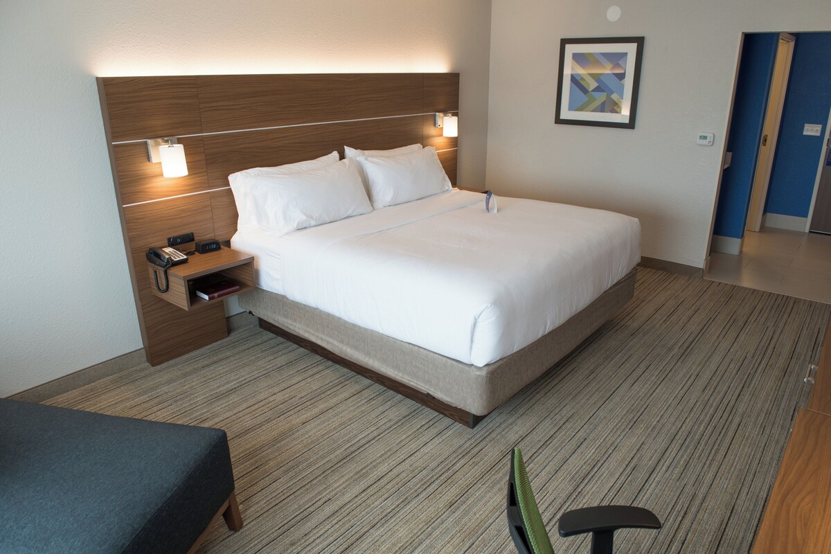 A hotel room with a bed, bedside table, lamp, and a small desk with a telephone.