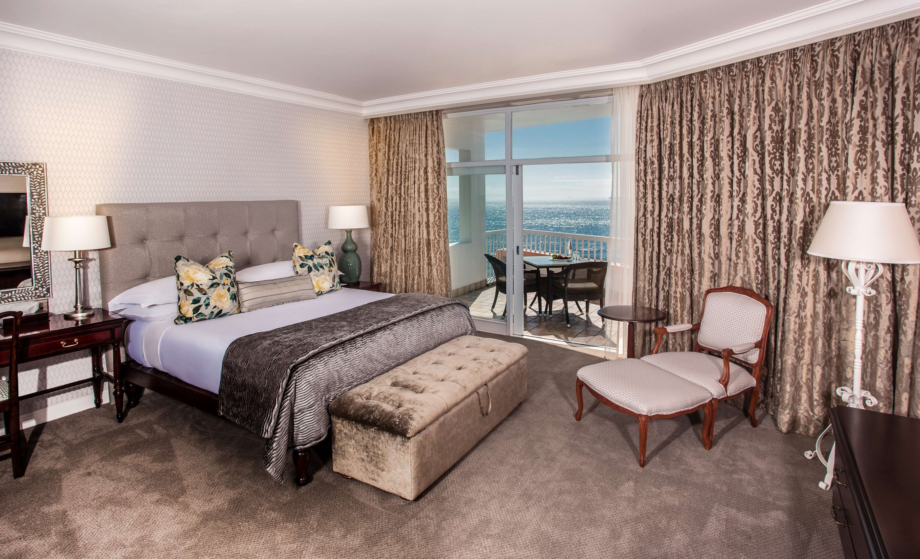 Habitación de hotel con una cama grande, un área de descanso con una silla, una mesita y un balcón con vistas.