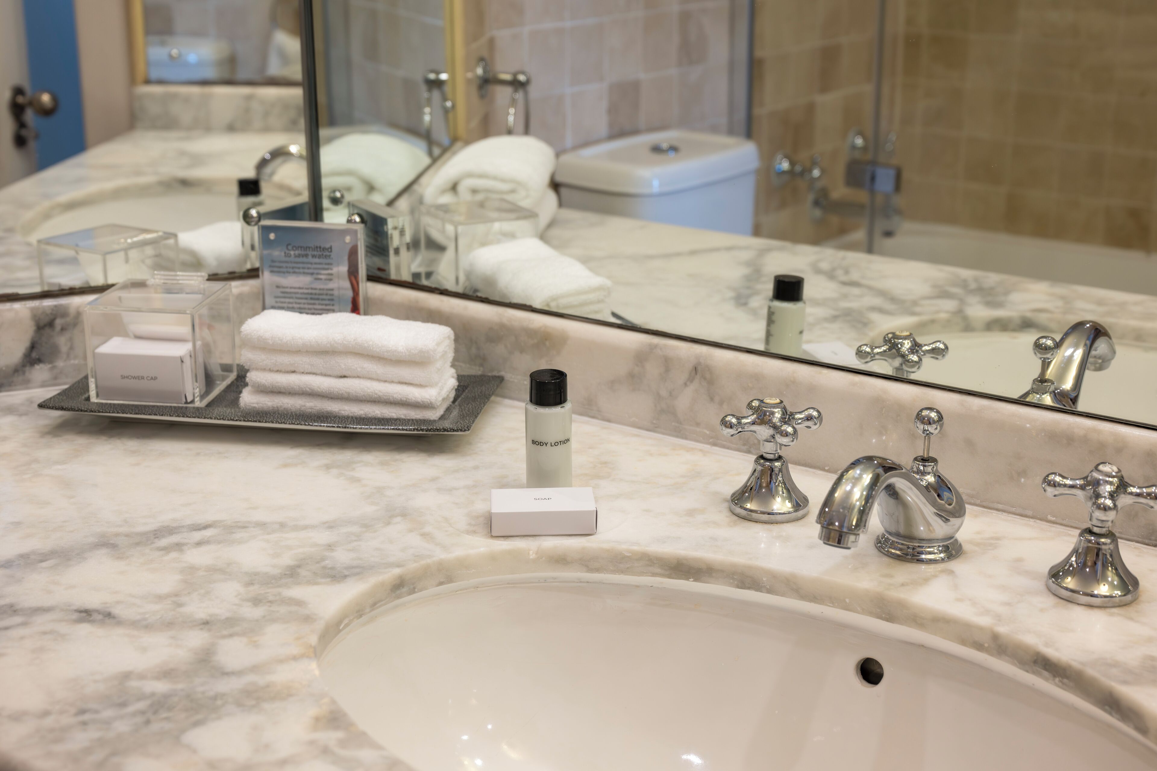 A bathroom with a marble sink, two faucets, a mirror, and toiletries on the counter.