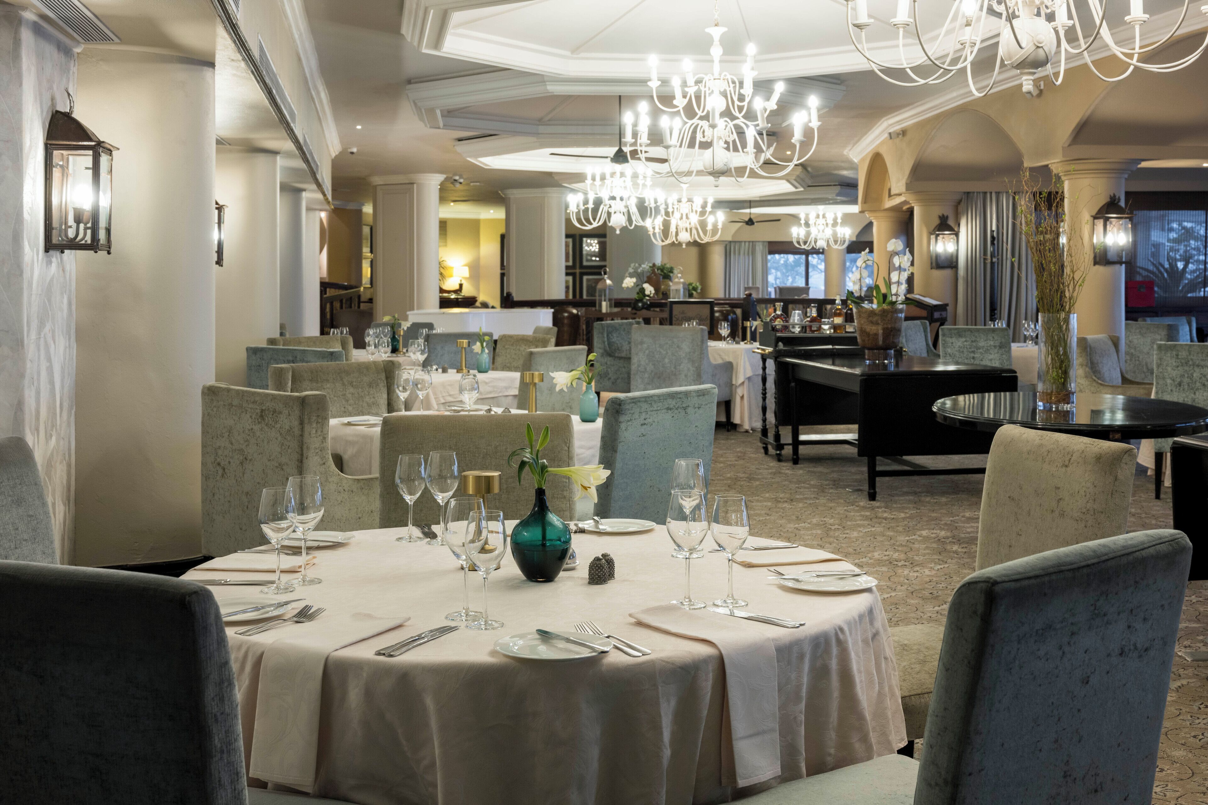 A dining area with round tables set for a meal, surrounded by upholstered chairs.