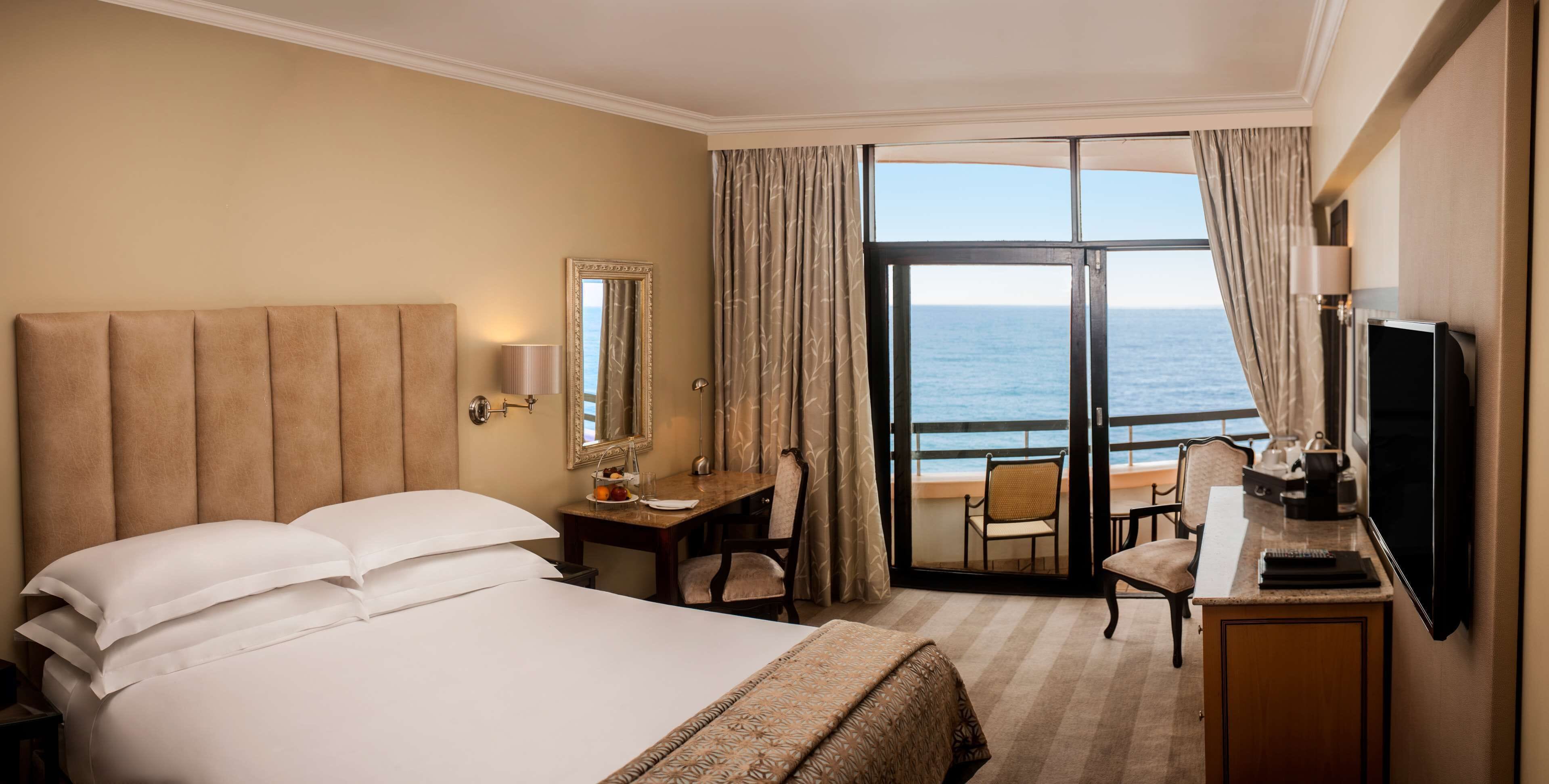 Una habitación de hotel con cama, escritorio, silla, televisor y vista al océano.