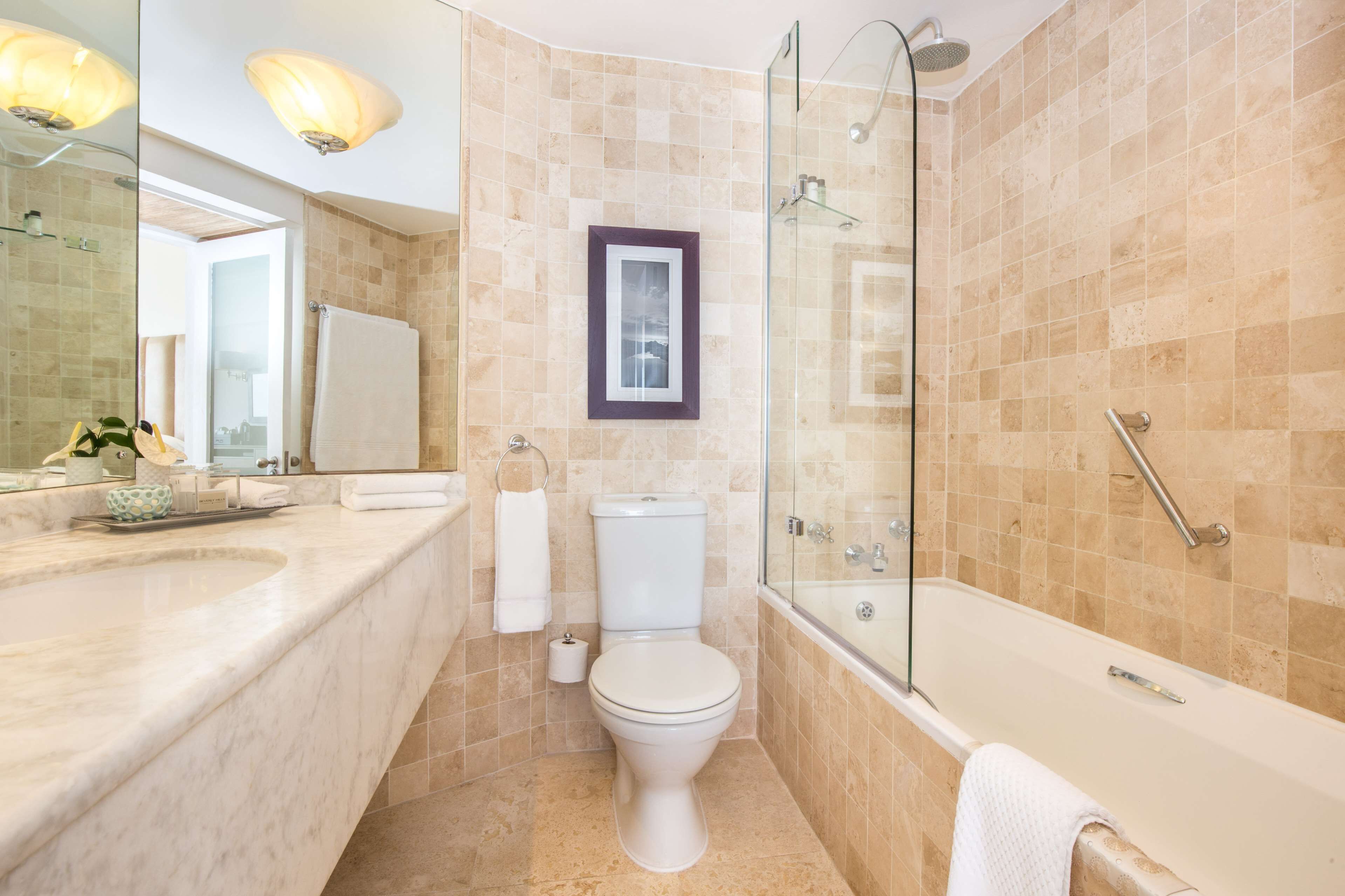Un baño moderno con ducha envuelta en vidrio, inodoro blanco y tocador de mármol.