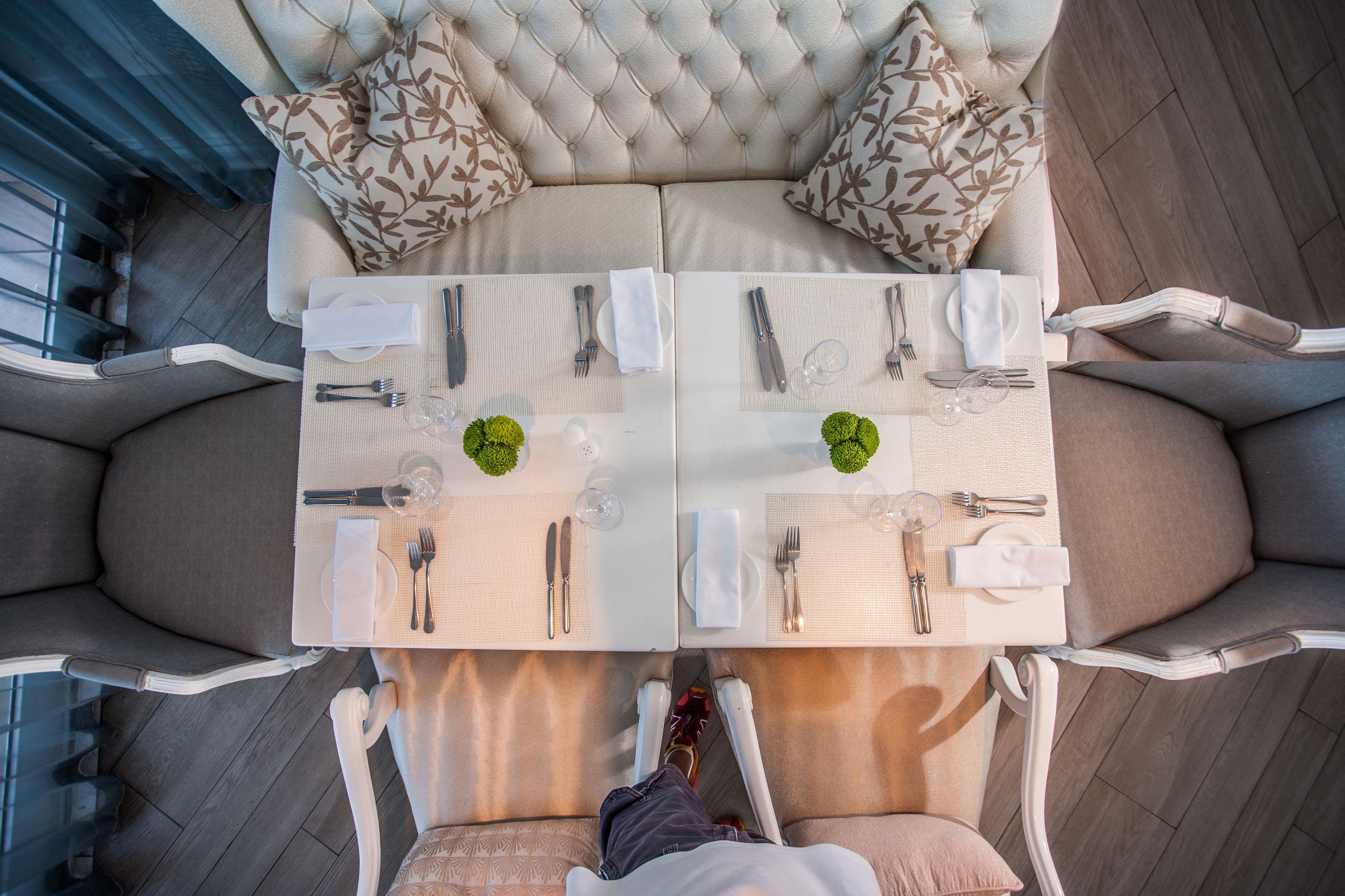A dining area with a tufted headboard sofa, two white dining tables set with cutlery and plates, and a view of the floor.
