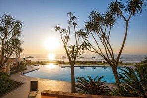 A pool area with palm trees, a view of the ocean, and a sunset. - Beverly Hills (uMhlanga)