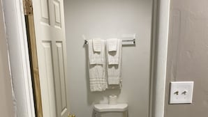 A bathroom with a toilet, a towel rack with two towels, and a visible light switch on the wall. - Tourist Inn (Absecon)