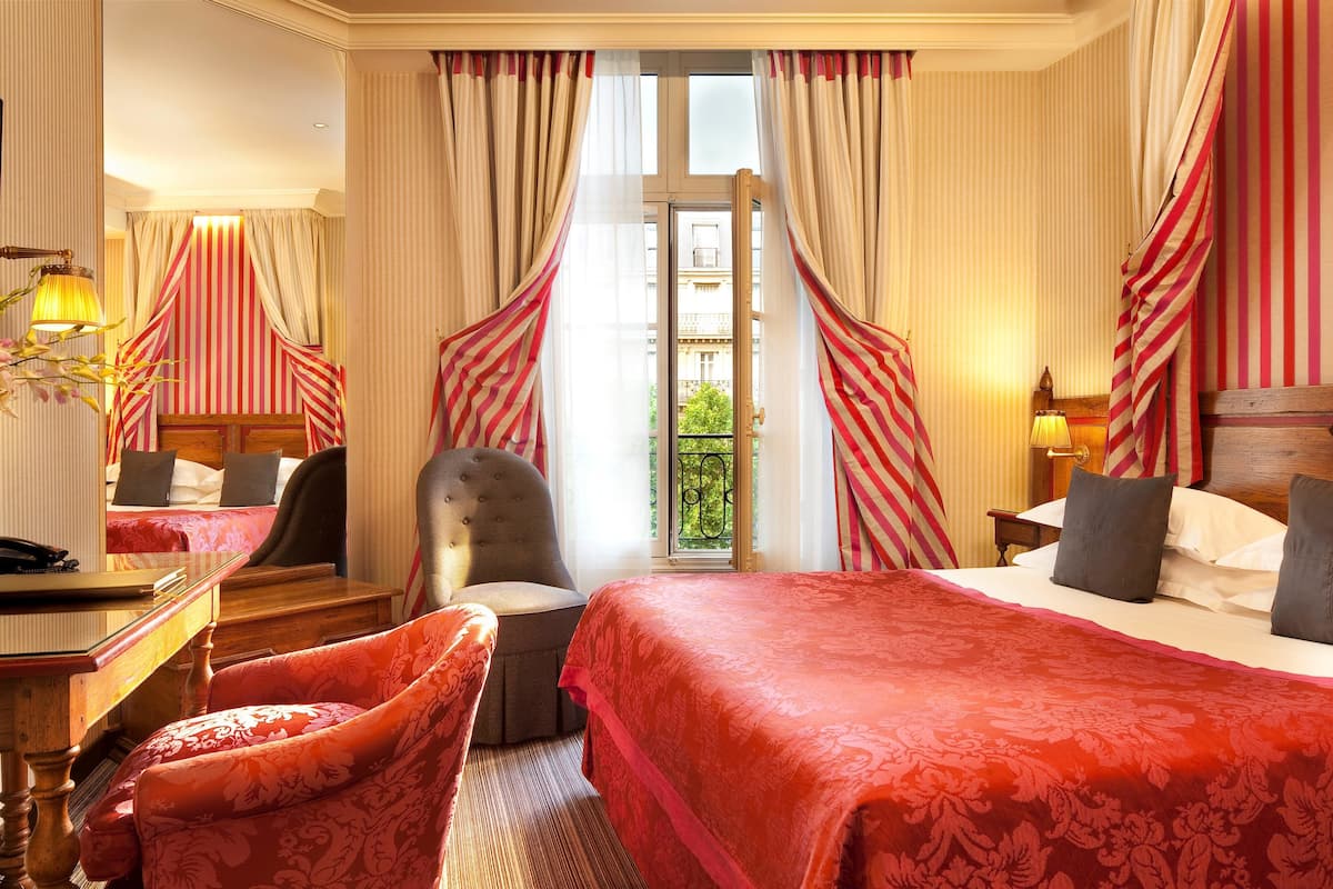Habitación de hotel con dos camas, un escritorio, una silla y vistas al balcón.