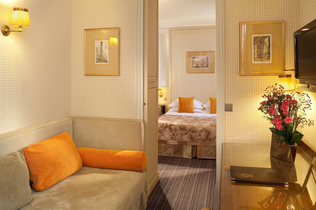 Habitación de hotel con sofá, cama, escritorio con lámpara y cuadros en las paredes.