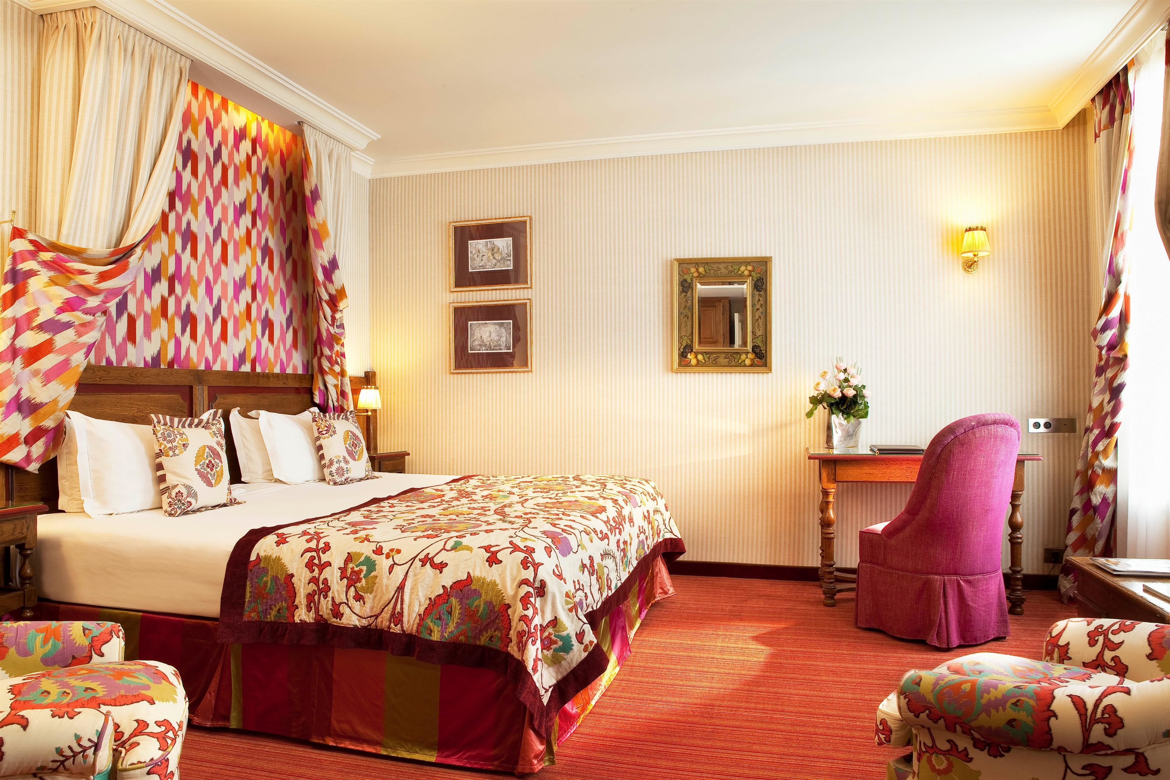 A hotel room with a large bed, a desk, a chair, and a mirror.