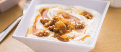 Un tazón blanco de yogur con salsa de caramelo y nueces sobre una mesa de madera.