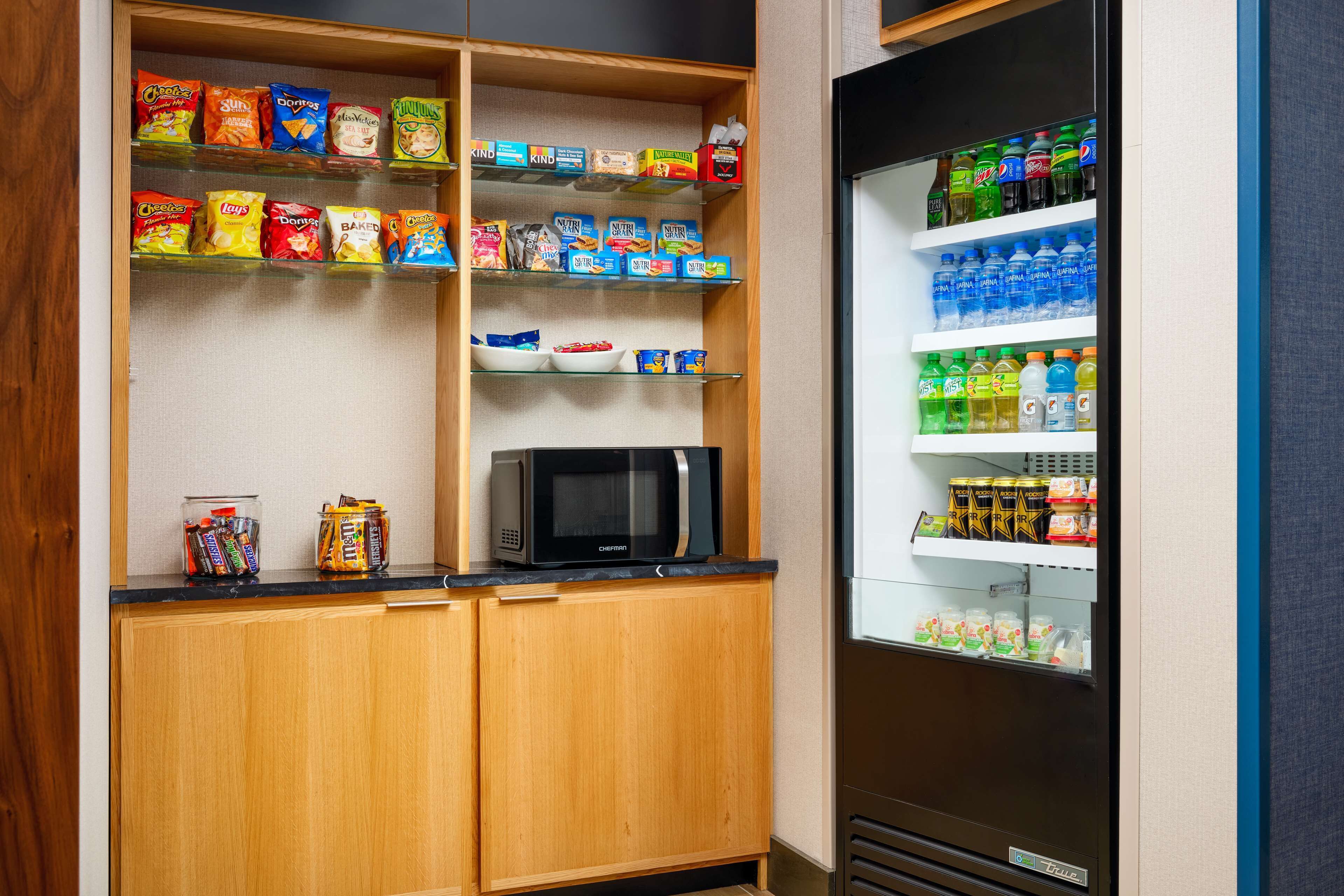 A compact kitchenette with a microwave, snack shelves, and a beverage fridge.