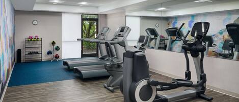 Ein Fitnessstudio mit Laufbändern, Crosstrainern und einem blauen Teppichboden.