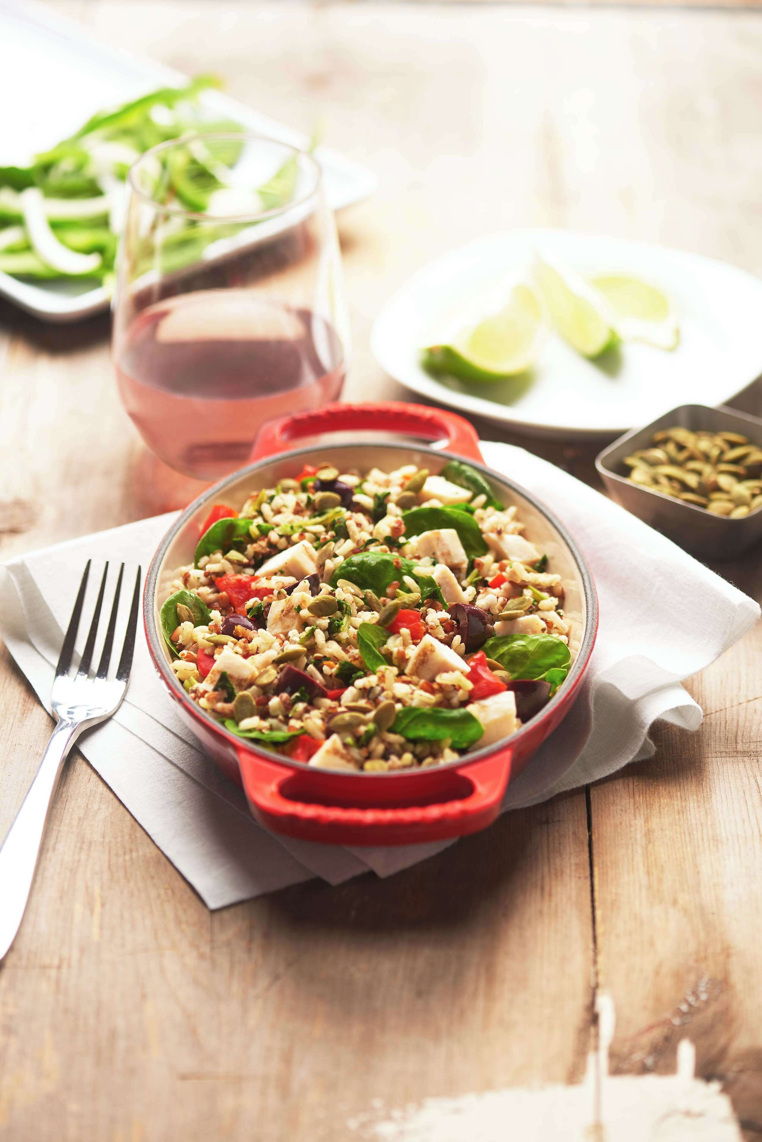 A salad in a red bowl on a wooden table with a fork and a glass of pink drink in the background.
