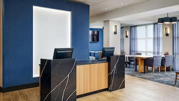 Una moderna zona de recepción de hotel con un mostrador de mármol, un panel decorativo de madera y una mesa de conferencias con sillas.