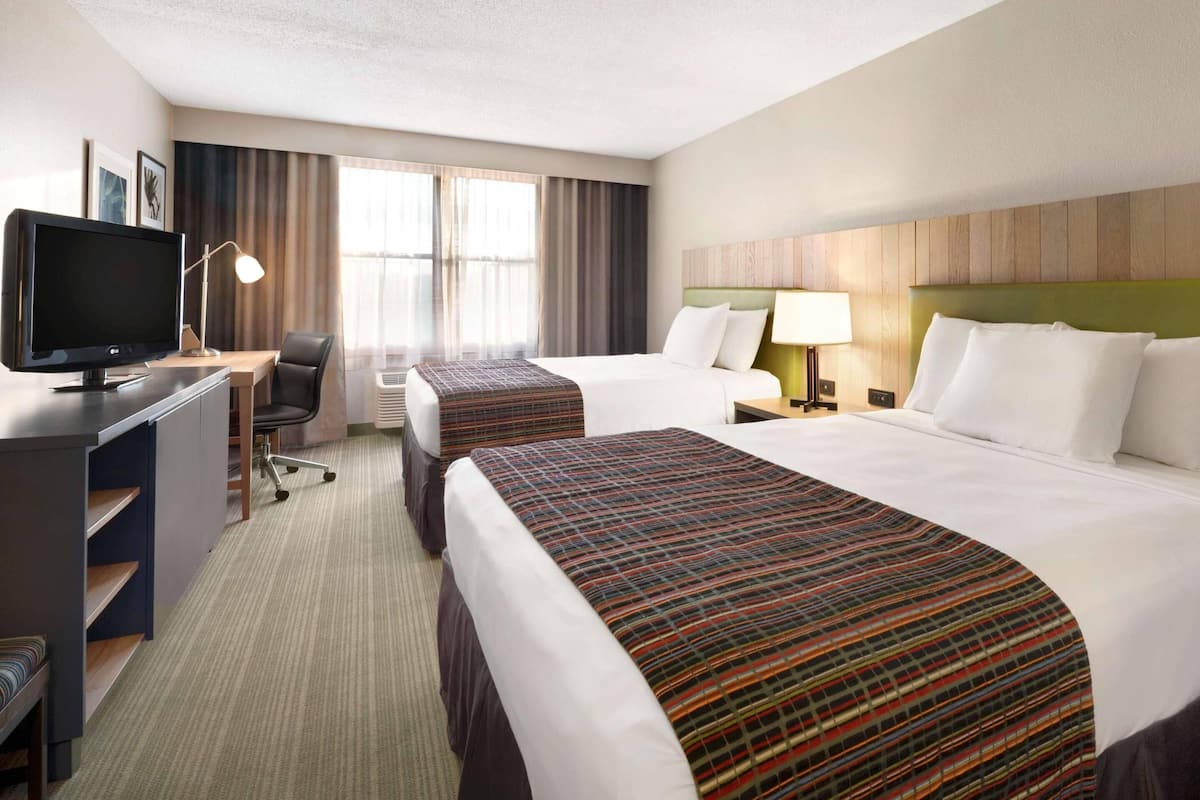 A hotel room with two beds, a desk with a computer, a chair, and a TV.