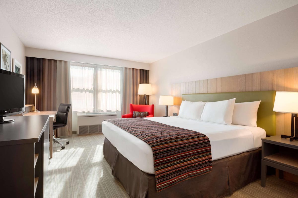 A hotel room with a large bed, a desk with a computer, a chair, and two bedside lamps.
