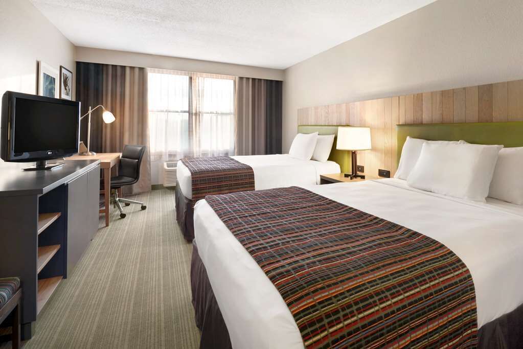A hotel room with two beds, a desk with a computer, a chair, a TV, and a window with curtains.