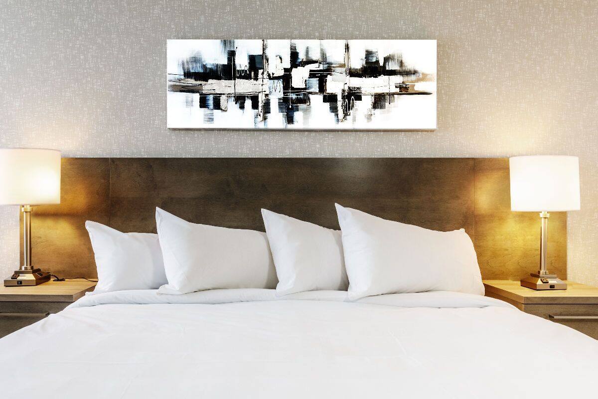 A hotel room with a large bed, two bedside lamps, a modern abstract painting, and a textured wall.