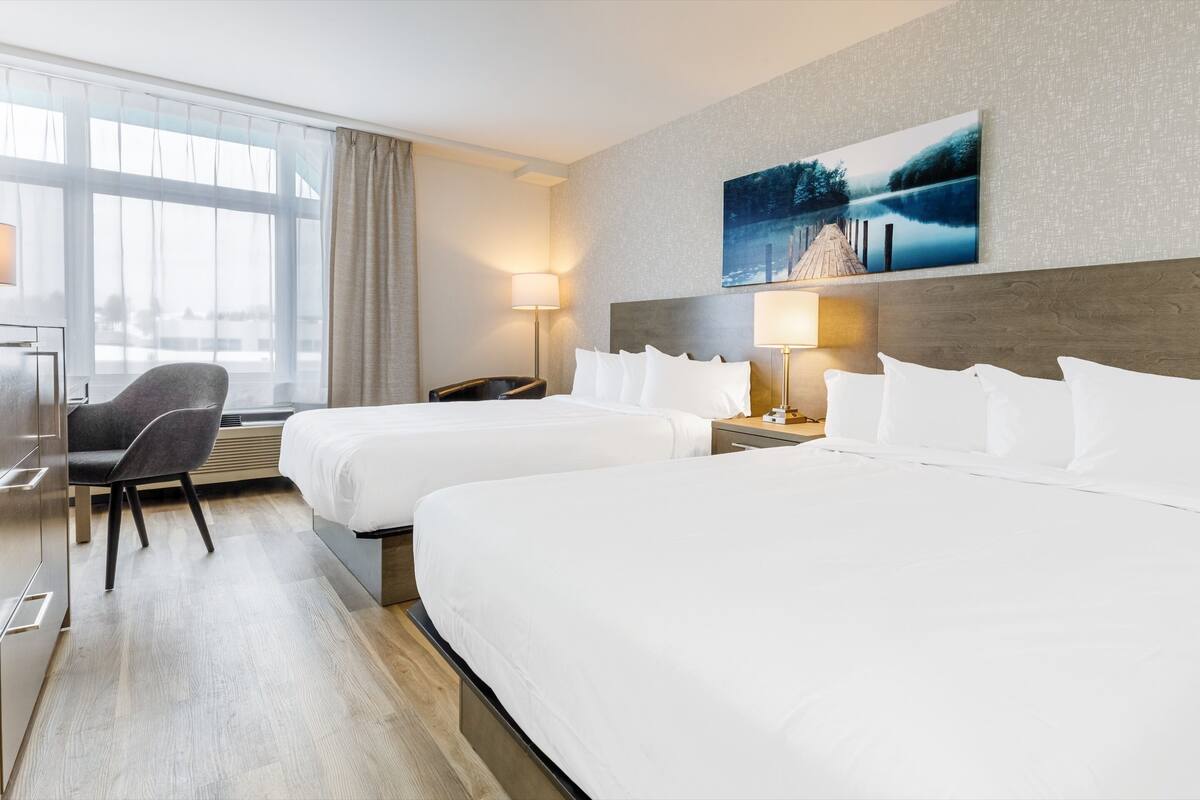 A hotel room with two beds, a desk, a chair, and a large window.
