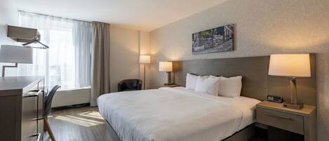 A hotel room with a large bed, bedside tables with lamps, a desk with a chair, and a window with curtains.