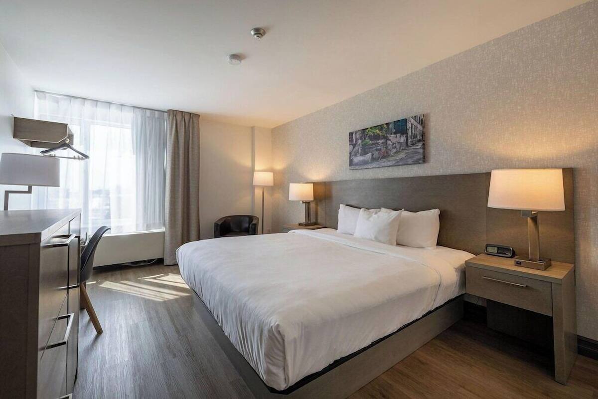 A hotel room with a large bed, bedside tables with lamps, a desk with a chair, and a window with curtains.