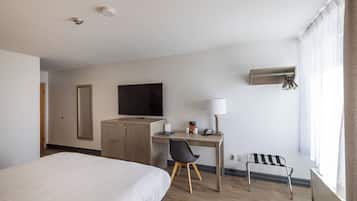 Habitación de hotel con una cama, un escritorio con silla, televisor, lámpara y ventana con cortinas.