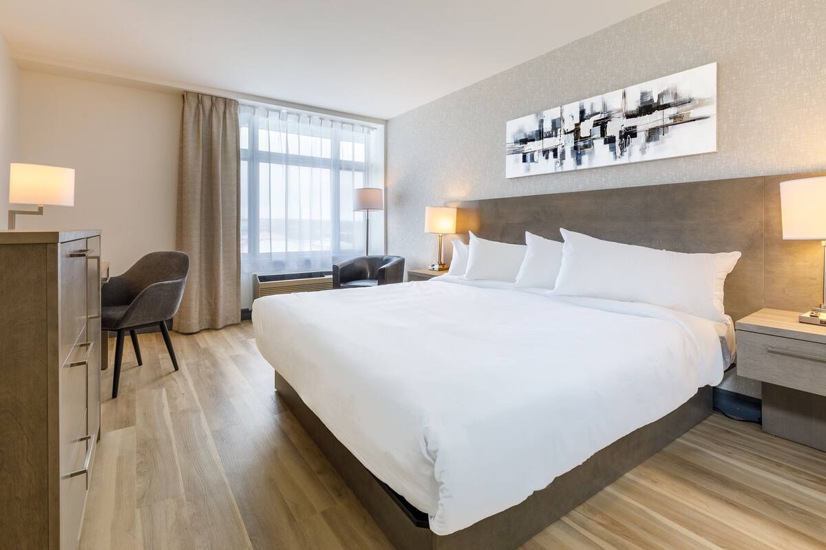 A hotel room with a large bed, bedside lamps, a desk, a chair, and a window with curtains.