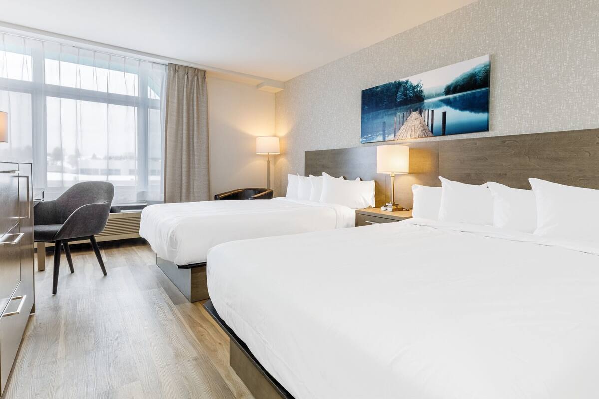 A hotel room with two beds, a desk, a chair, and a large window.
