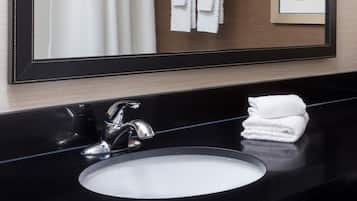 Un baño con encimera negra, lavamanos blanco, grifo plateado y espejo con marco negro.