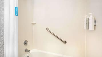 A bathroom with a bathtub, a shower, and a handrail. There are toiletries on the wall.