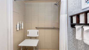 A shower area with a white chair, a handrail, and a shelf with towels.