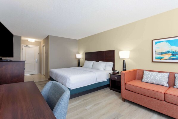 A hotel room with a bed, a desk, a chair, a sofa, and a painting on the wall. - Hampton Inn Orlando-International Airport (Orlando)